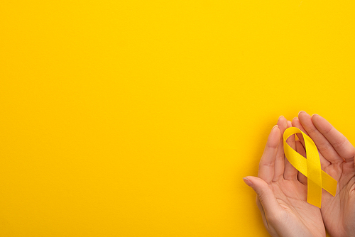 Cropped view of female hands with yellow awareness ribbon on colorful background, international childhood cancer day concept