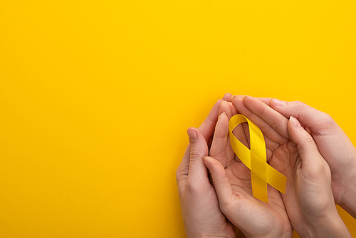Cropped view of woman and man holding yellow ribbon on colorful background, international childhood cancer day concept