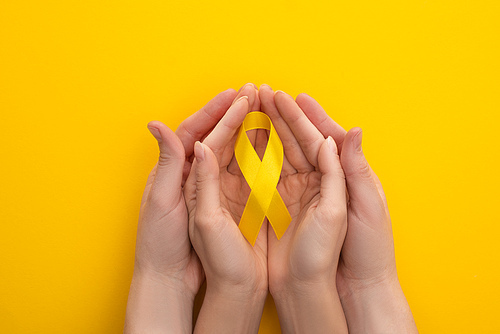 Cropped view of male and female hands with yellow ribbon on colorful background, international childhood cancer day concept