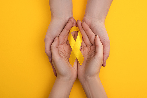 Cropped view of couple holding yellow ribbon on colorful background, international childhood cancer day concept