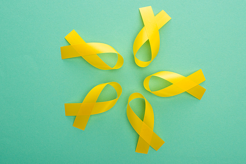 Top view of yellow awareness ribbons on turquoise background, international childhood cancer day concept