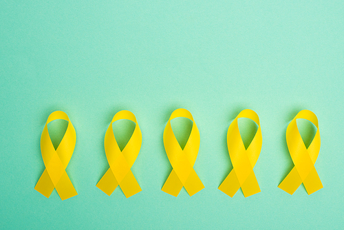 Flat lay with yellow awareness ribbons on turquoise background, international childhood cancer day concept