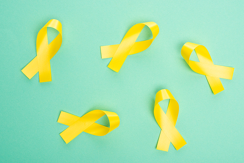 Top view of yellow ribbons on turquoise background, international childhood cancer day concept