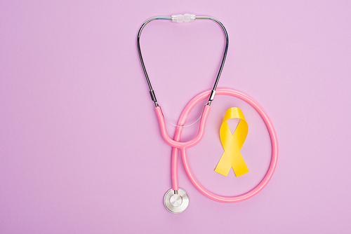 Top view of yellow ribbon with pink stethoscope on violet background, international childhood cancer day concept