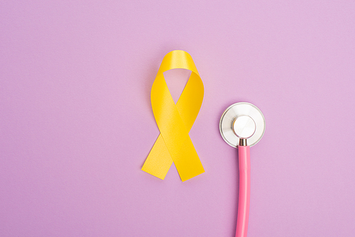 Top view of yellow ribbon with stethoscope on violet background, international childhood cancer day concept
