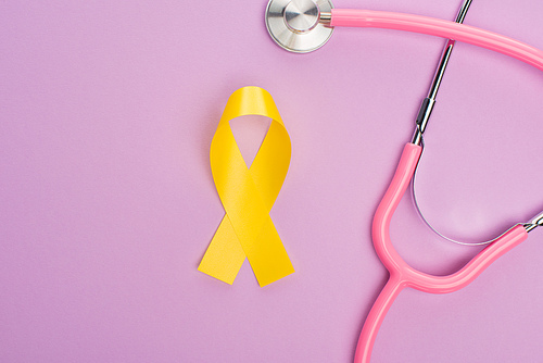 Top view of yellow ribbon and stethoscope on violet background, international childhood cancer day concept
