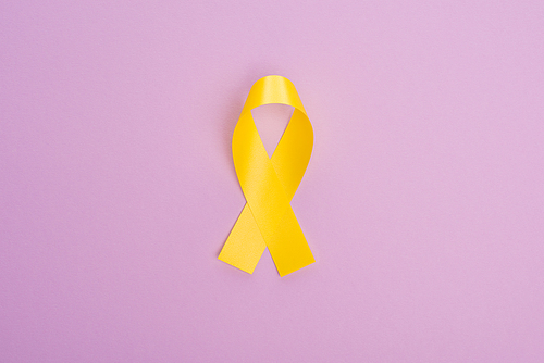 Top view of yellow ribbon on violet background, international childhood cancer day concept