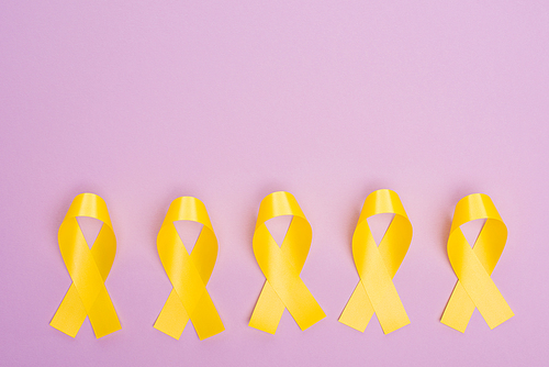 Flat lay with yellow awareness ribbons on violet, international childhood cancer day concept