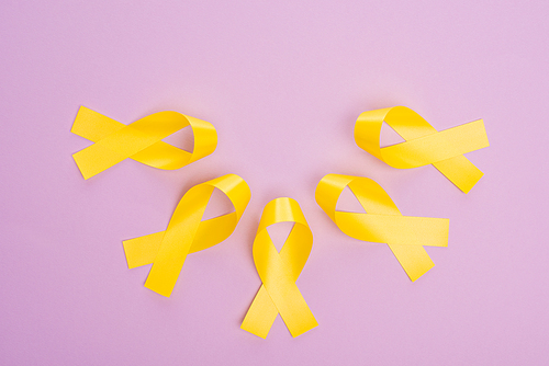 Flat lay with yellow ribbons on violet background, international childhood cancer day concept