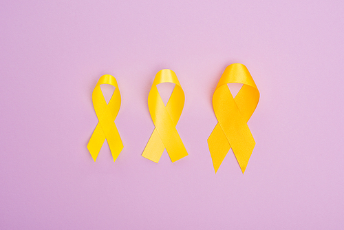 Top view of yellow awareness ribbons on violet background, international childhood cancer day concept