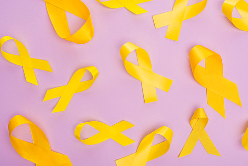 Top view of yellow ribbons on violet background, international childhood cancer day concept