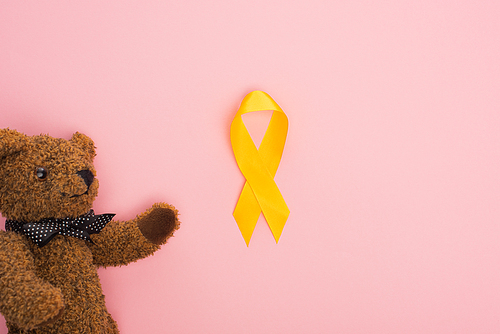 Top view of yellow ribbon and toy on pink background, international childhood cancer day concept