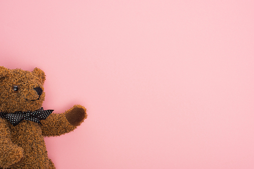 Top view of brown teddy bear with bow on pink background