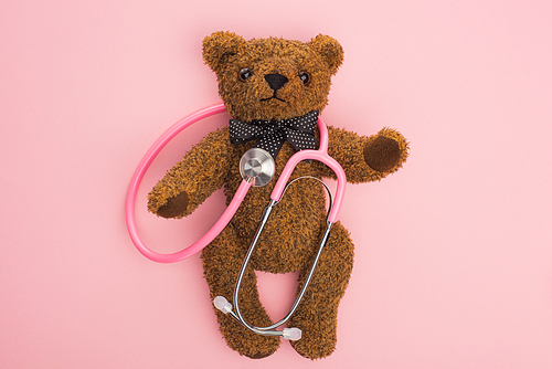 Top view of stethoscope on teddy bear on pink background, international childhood cancer day concept