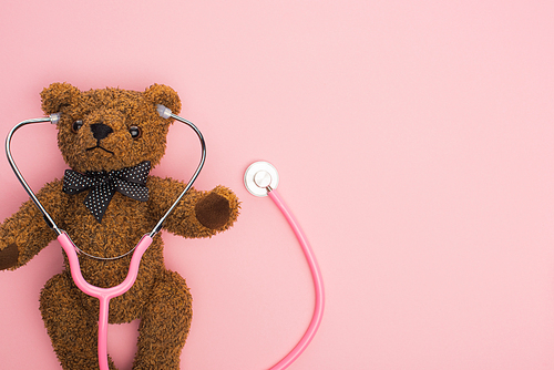Top view of stethoscope with teddy bear on pink background, international childhood cancer day concept