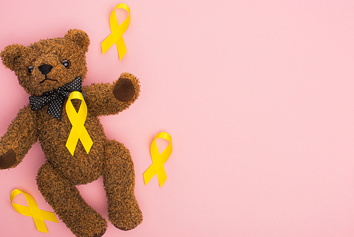 Top view of yellow awareness ribbons and teddy bear on pink background, international childhood cancer day concept