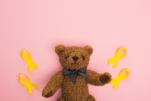 Top view of yellow ribbons with toy on pink background, international childhood cancer day concept