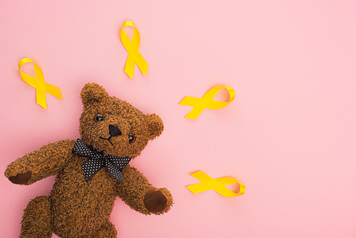 Top view of yellow ribbons near teddy bear on pink, international childhood cancer day concept