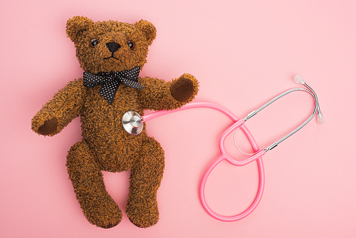 Top view of stethoscope connected with teddy bear on pink background, international childhood cancer day concept