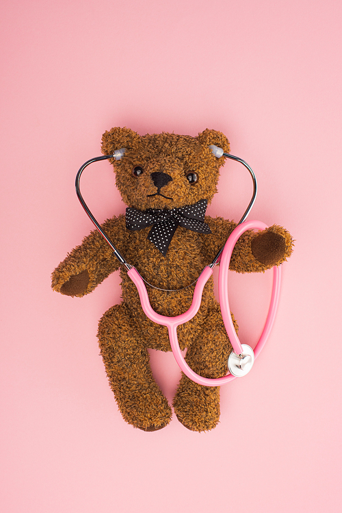 Top view of teddy bear with stethoscope on pink background, international childhood cancer day concept