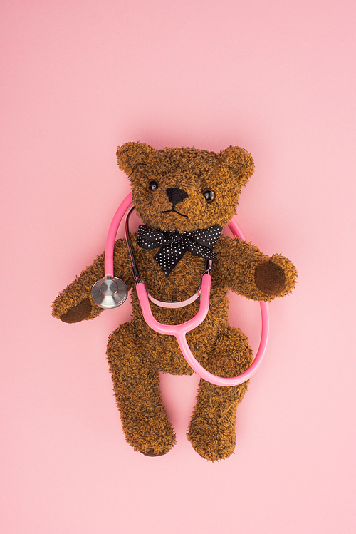 Top view of brown teddy bear with stethoscope on pink, international childhood cancer day concept