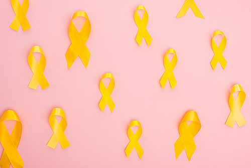 Top view of yellow ribbons on pink background, international childhood cancer day concept