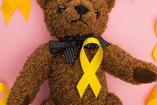 Top view of yellow ribbons with teddy bear on pink background, international childhood cancer day concept