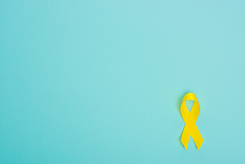 Top view of yellow ribbon on blue background, international childhood cancer day concept