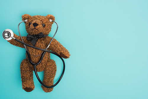 Top view of brown teddy bear with stethoscope on blue background, international childhood cancer day concept