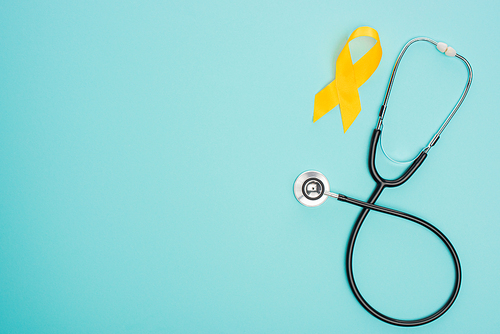 Top view of yellow ribbon with stethoscope on blue background, international childhood cancer day concept