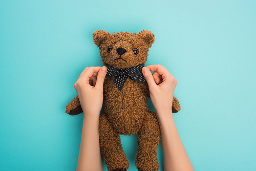 Cropped view of woman straightening bow on teddy bear on blue background