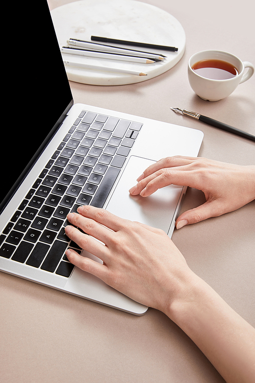 cropped view of woman using laptop near cup of tea on beige surface