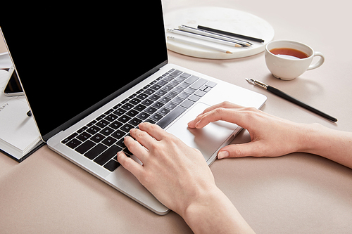 cropped view of woman using laptop near cup of tea on beige surface