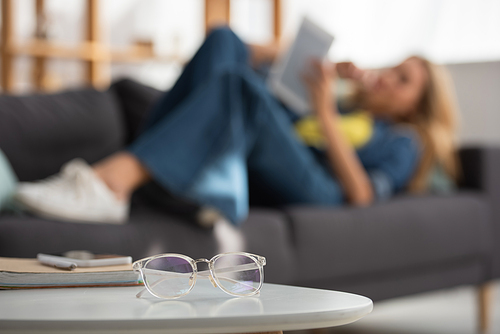 Eyeglasses on coffee table with blurred woman on background