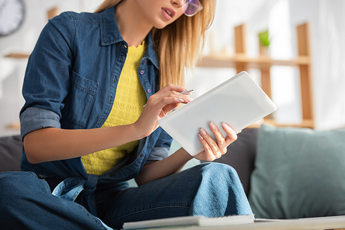 Cropped view of young woman using digital tablet at home on blurred background