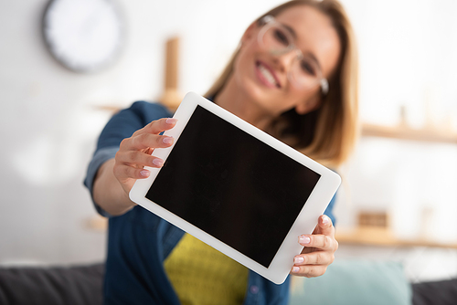 Happy blonde woman  while showing digital tablet on blurred background