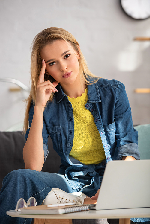 Young blonde woman  while sitting on couch at home on blurred background