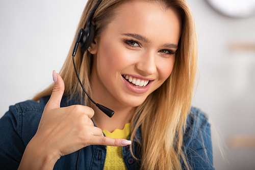 Portrait of cheerful blonde woman  while showing call gesture on blurred background