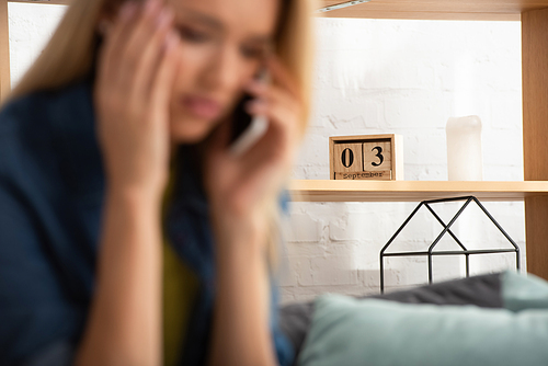 Wooden calendar on shelf with blurred worried woman talking on smartphone on foreground