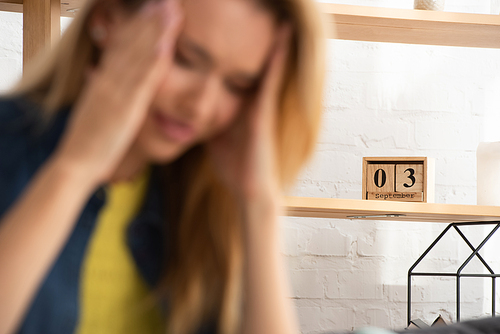 Wooden calendar on shelf with blurred tense woman on foreground