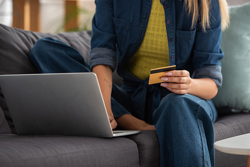 Cropped view of young woman with credit card using laptop on blurred background