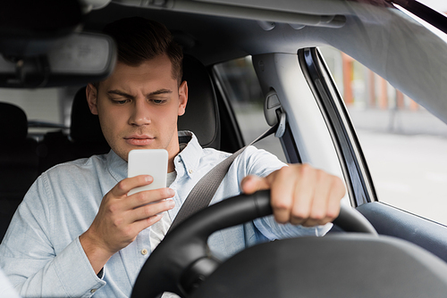 young man chatting on smartphone while driving car, blurred foreground