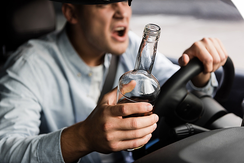 cropped view of aggressive, drunk man with bottle of whiskey shouting while driving car