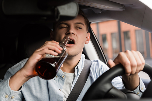 drunk man driving car and drinking whiskey on blurred foreground