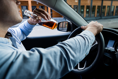 cropped view of man drinking whiskey while driving car, blurred foreground