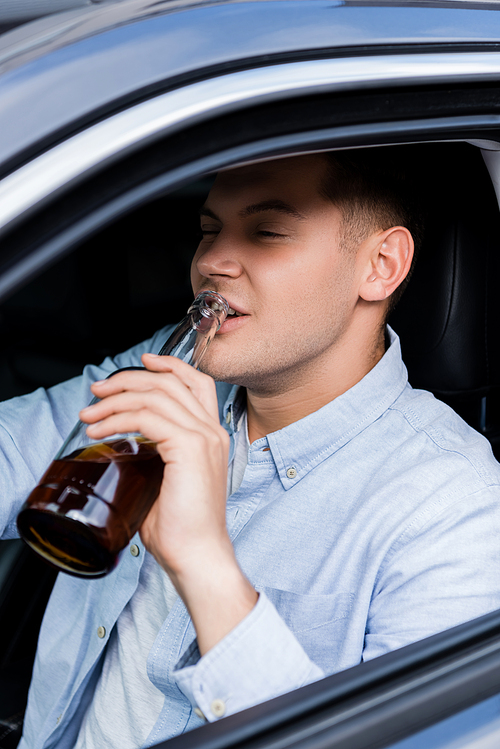 young man drinking whiskey while driving car on blurred foreground