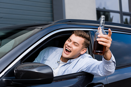 excited, drunk man with bottle of whiskey shouting while looking out car window