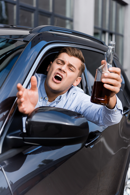 drunk, angry man with bottle of alcohol gesturing and shouting while looking out car window, blurred foreground