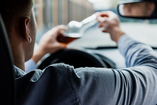 partial view of man opening bottle of alcohol in car, blurred foreground