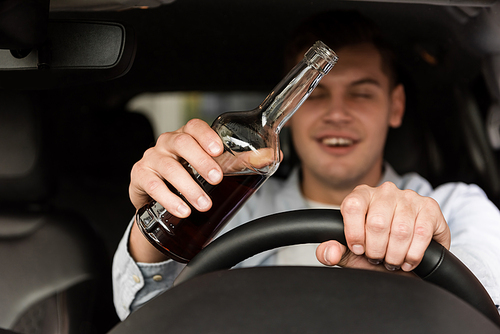 drunk man with bottle of whiskey driving car on blurred background